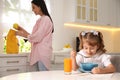 Little girl having breakfast while mother helping her get ready for school in kitchen Royalty Free Stock Photo