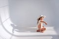 Little girl is having fun on the floor in stylish hat in a white loft interior with airy fabrics Royalty Free Stock Photo