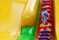 A little girl is having fun on a high inflatable slide and climbs up the stairs. A small child is having fun on an inflatable tram