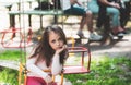 Little girl having fun on a swing outdoor. Sad girl sitting alone on a swing in a park playground. Charming stylish Royalty Free Stock Photo