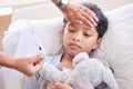 Little girl having her temperature taken with a thermometer by her mother at home. Small sick child lying in bed holding Royalty Free Stock Photo