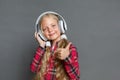 Little girl in headphones with ponytails standing isolated on grey listneing music thumb up looking camera delightful Royalty Free Stock Photo