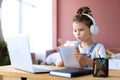 Little girl in headphones sit at desk writing in notebook studying online do exercises at home Royalty Free Stock Photo