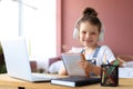 Little girl in headphones sit at desk writing in notebook studying online do exercises at home Royalty Free Stock Photo