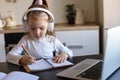 Little girl in headphones sit at desk writing in notebook studying online do exercises at home Royalty Free Stock Photo