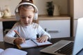 Little girl in headphones sit at desk writing in notebook studying online do exercises at home Royalty Free Stock Photo