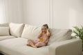 Little girl with headphones sitting on comfortable sofa in living room Royalty Free Stock Photo