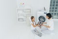 Little girl helper and her mother pose in laundry room near washing machine, sit on white floor, hold dirty shirt, do washing at Royalty Free Stock Photo