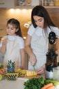 Little girl helps her mom in the kitchen. Women slice ananas for fresh homemade juice Royalty Free Stock Photo