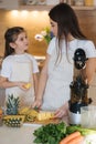 Little girl helps her mom in the kitchen. Women slice ananas for fresh homemade juice Royalty Free Stock Photo