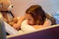 Little girl with her bear reading a book in the bedroom Royalty Free Stock Photo