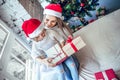 A little girl with her mom opens a New Year`s gift near a festive Christmas tree Royalty Free Stock Photo