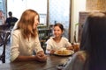 Little girl and her mother eating sweet belgian waffles with banana and cream in a cafe, daughter making a funny face Royalty Free Stock Photo