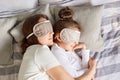 Little girl and her mother enjoying morning sleeping together hugging wearing blindfolds having day napping together in bedroom