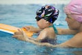 Little girl and her mother making excercises with float board in the swimming pool