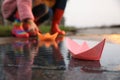 Little girl and her mother playing near puddle outdoors, focus on paper boat Royalty Free Stock Photo