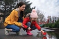 Little girl and her mother playing with paper boat near puddle outdoors Royalty Free Stock Photo