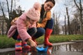 Little girl and her mother playing with paper boat near puddle in park Royalty Free Stock Photo