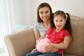 Little girl with her mother sitting on sofa and holding piggy bank indoors. Money savings concept Royalty Free Stock Photo