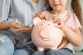 Little girl with her mother sitting on sofa and putting coin into piggy bank, closeup. Money savings concept