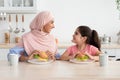 Little Girl And Her Muslim Mom In Hijab Eating Sandwiches In Kitchen