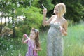 Little girl with her pregnant mommy have fun blowing bubbles in park Royalty Free Stock Photo