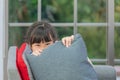 Girl hiding behind pillow with smile and playful face on a gray sofa in livingroom Royalty Free Stock Photo