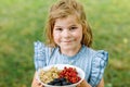 Little girl holdig Red currants, white currants and blackberries in a bowl in sunny summer garden. Healthy nutrition for