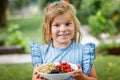 Little girl holdig Red currants, white currants and blackberries in a bowl in sunny summer garden. Healthy nutrition for