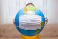 The little girl is holding the earth globe in her hands. Surgical mask on earth globe