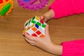 A little girl holding a Rubik& x27;s cube on a wood background.