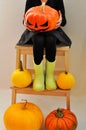 The little girl is holding a scary pumpkin for Halloween, sitting on a bench surrounded by other pumpkins. Closup