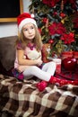 A little girl holding a Teddy bear, sitting on a plaid blanket in the Christmas decorations near a Christmas tree with boxes of gi Royalty Free Stock Photo
