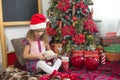 A little girl holding a Teddy bear, sitting on a plaid blanket in the Christmas decorations near a Christmas tree with boxes of gi Royalty Free Stock Photo