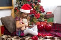 A little girl holding a Teddy bear, sitting on a plaid blanket in the Christmas decorations near a Christmas tree with boxes of gi Royalty Free Stock Photo