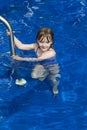 Little girl holding unto railing to step into deep blue pool