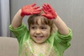 A little girl holds her hands above her head, which are smeared with children`s hand paints. Concept: development of creativity an