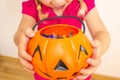 A little girl holds a pumpkin with candy in her hands and stretches it to get even more candies for Halloween. Close-up. Royalty Free Stock Photo