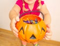 A little girl holds a pumpkin with candy in her hands and stretches it to get even more candies for Halloween. Close-up. Royalty Free Stock Photo