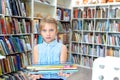 Little girl holds stack of books with fairy tales in children`s library. Special reading kids room. Shelves with bright