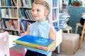 Little girl holds stack of books with fairy tales in children`s library. Special reading kids room. Shelves with bright Royalty Free Stock Photo