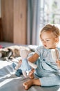 Little girl holds a teddy bear in her outstretched hand with a comb in her other hand while sitting on the bed Royalty Free Stock Photo