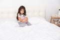 Little girl in home wear sits with teddy bunny on bed at home