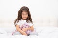 Little girl in home wear sits with teddy bunny on bed at home