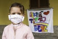 Little girl with homemade face protective mask. Blurred background with the famed rainbow drawing and the message
