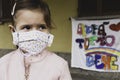 Little girl with homemade face protective mask. Blurred background with the famed rainbow drawing and the message