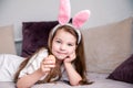 Little girl in a hoop in the form of rabbit ears lies on a sofa at home and poses with a chicken egg in her hand Royalty Free Stock Photo