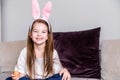 Little girl in a hoop in the form of rabbit ears sit on a sofa at home and poses with a chicken egg in her hand Royalty Free Stock Photo