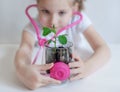 Little girl imagining herself as doctor while playing with pink stethoscope. Young plants. Caring for a new life. Climate change