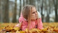 A little girl indifferently lies on the autumn foliage in a city park. She is very sad. Royalty Free Stock Photo